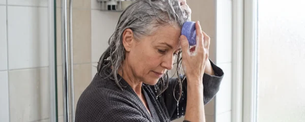 Femme aux cheveux blancs massant ses racines avec un shampoing solide bleu sous la douche